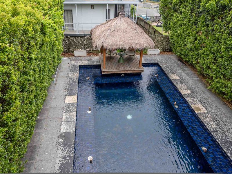 A traditional Balinese-style hut with a thatched roof sits at the water's edge on a timber deck, providing a shaded spot for relaxation.