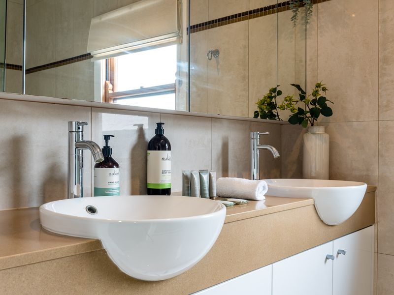 The spacious bathroom features a large vanity with twin vessel sinks and extensive under-bench cabinetry.