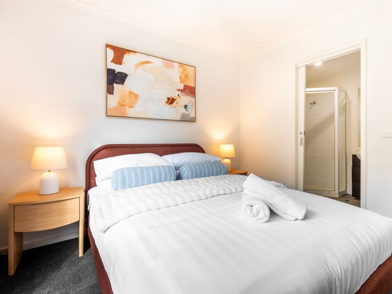 Spacious queen bedroom with soft furnishings and warm styling