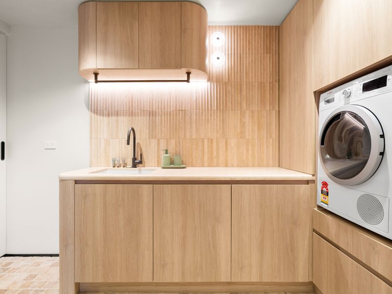Functional laundry with washer, sink, and generous bench space.
