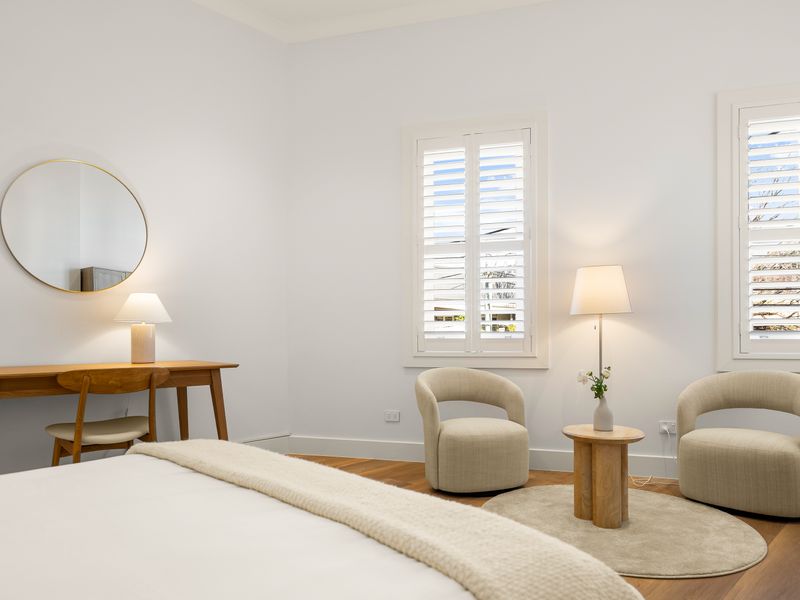 Peaceful bedroom with two armchairs and plantation shutters.