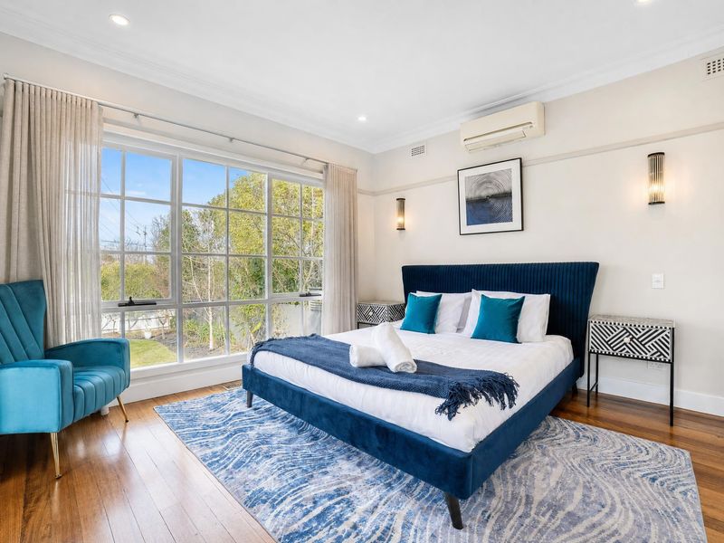 Spacious main bedroom with a plush blue bed and bright windows.