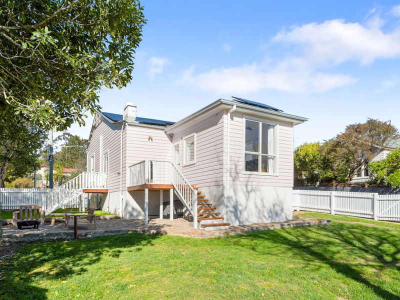 Exterior shot of the white cottage-style house set against a lush green lawn.