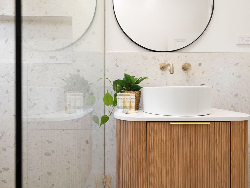 Contemporary bathroom vanity featuring a round mirror and wooden basin counter.