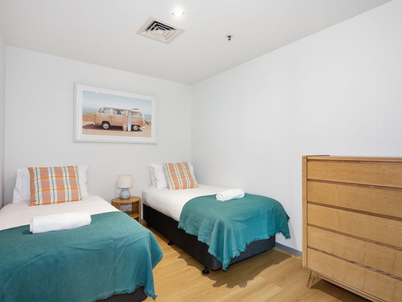 Bright twin bedroom setup featuring two single beds and a wooden dresser.