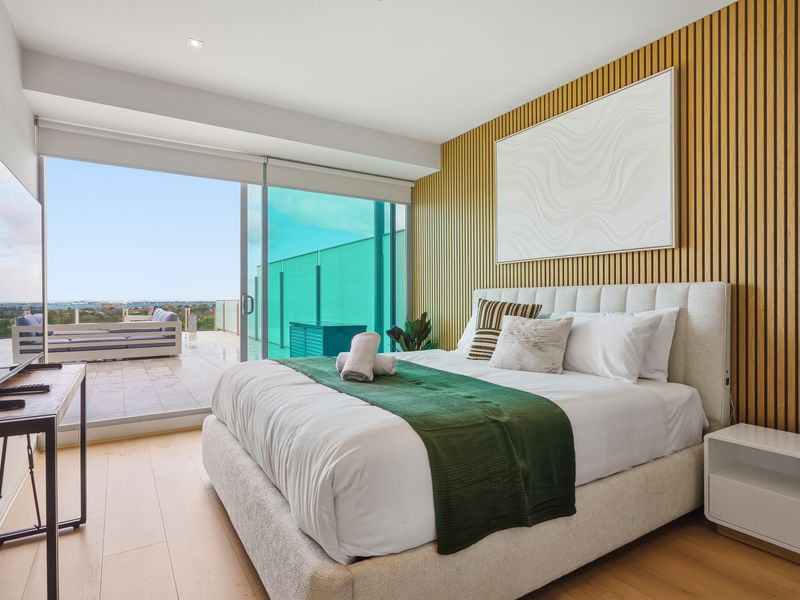 Modern bedroom featuring a plush bed, panel accent wall, and direct balcony access.