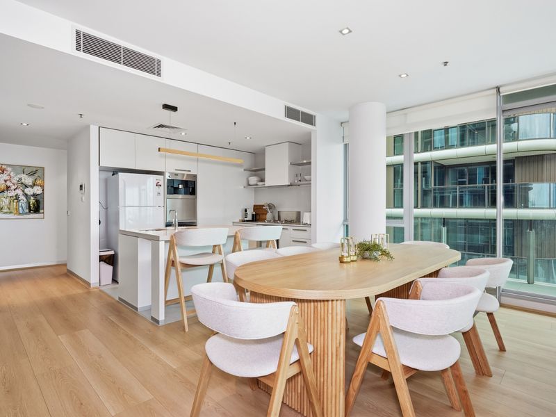 Open-plan dining and kitchen layout with a wooden table, chairs, and modern lighting.