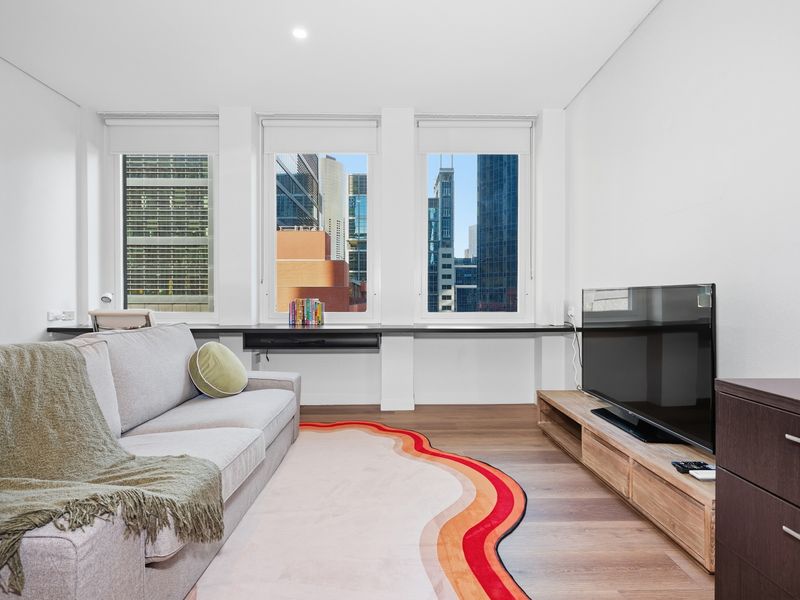 Bright living space with a grey couch, television, and city window views.