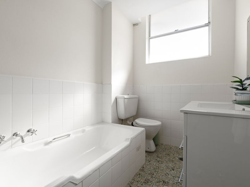 A compact all-white bathroom with a modern tub, vanity cabinet, and tiled accents under bright window lighting.