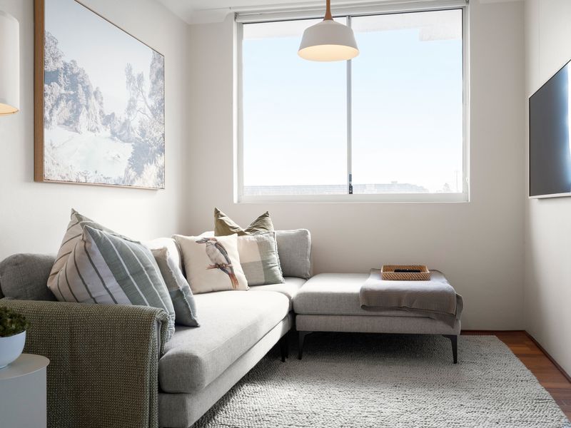 A compact apartment living room featuring a modern gray L-shaped sofa under a large window.