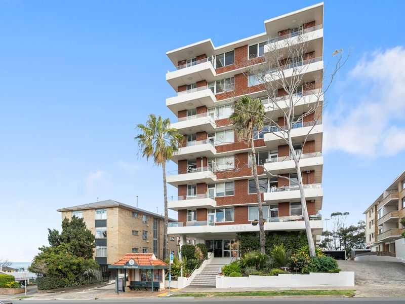 A mid-century modern high-rise apartment building with white balconies and brown brickwork under a clear sky.