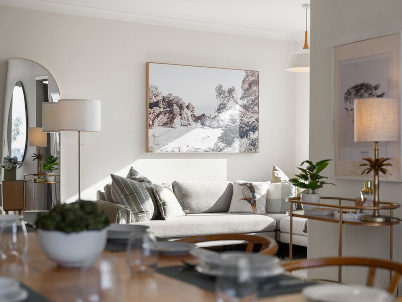 An elegantly arranged dining table in the foreground looking into a bright, contemporary open-concept living area with a grey sofa and large artwork.