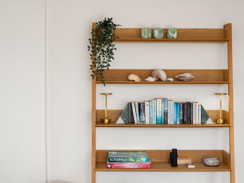 A wooden ladder shelf decorated with books, plants, and ocean-themed decor against a plain white wall.