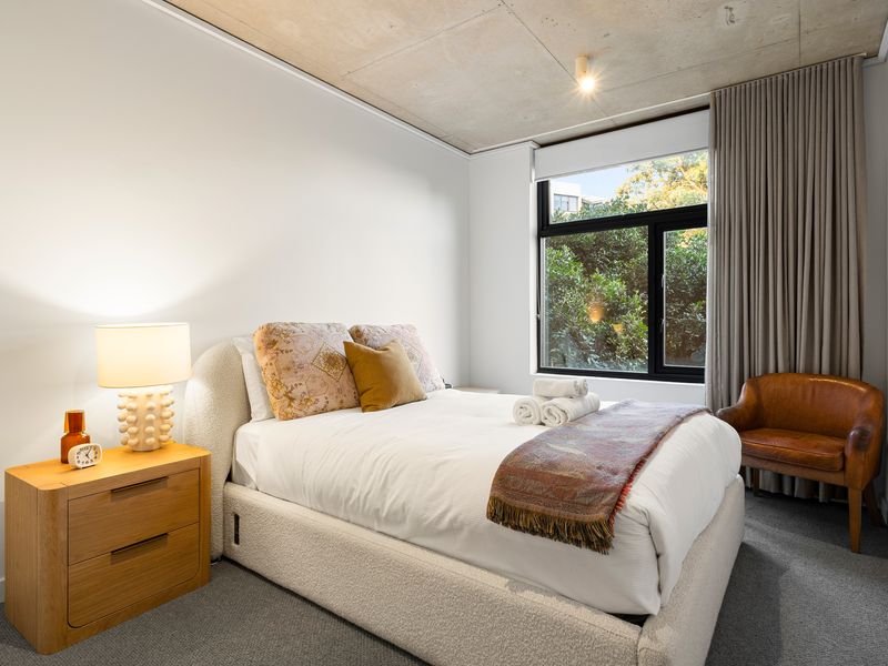 Light-filled bedroom featuring a neatly made bed, minimalist decor, and a large window framing outdoor views.