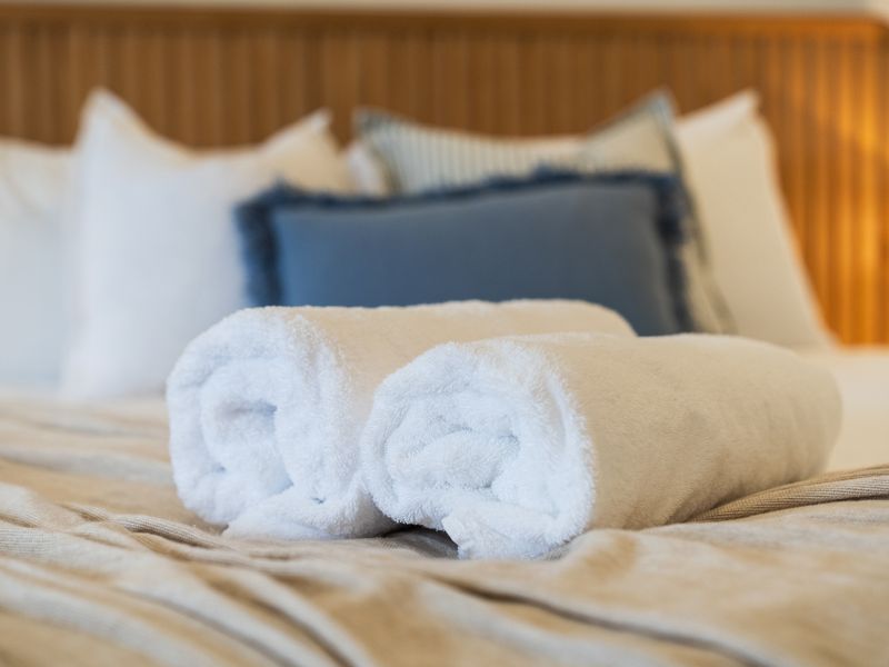 Cozy bed styling highlighting crisp white linens, rolled towels, and decorative pillows.