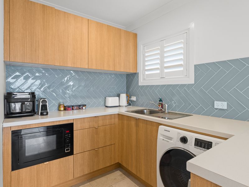 Modern kitchen featuring warm wooden cabinetry, a built-in oven, and a washing machine unit.