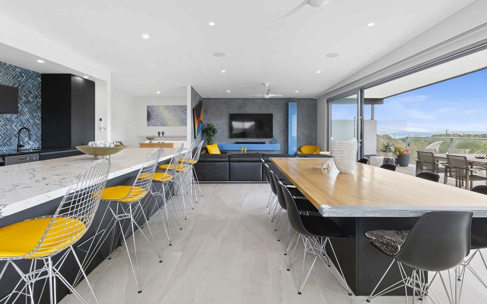 Open plan living, dining, and kitchen area with bay views, opening onto the deck featuring a spa and outdoor entertaining space.