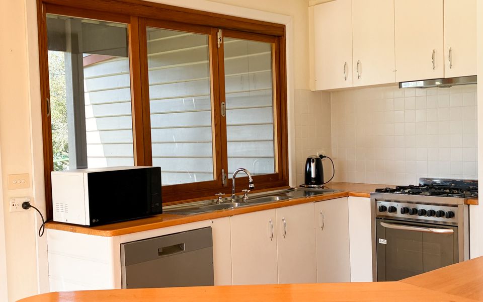Bright kitchen with bifold windows onto the deck, coffee machine, microwave, dishwasher and oven.