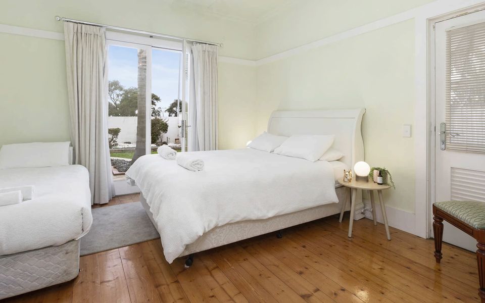 Bedroom 2 with Queen bed and single bed. French doors open onto the landscaped front garden