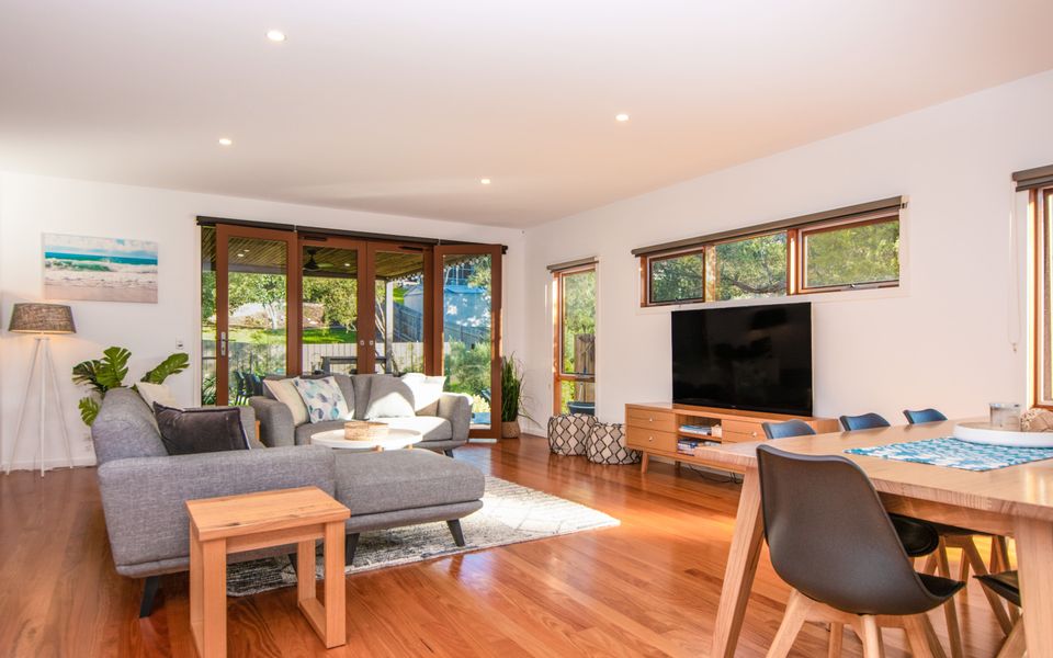 Lounge area with TV and floor to ceiling glazed doors opening onto the rear deck.