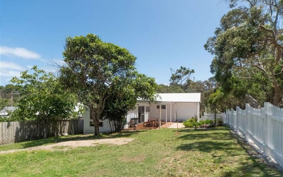 Large yard is surrounded by a white picket fence and lots of trees for extra privacy.