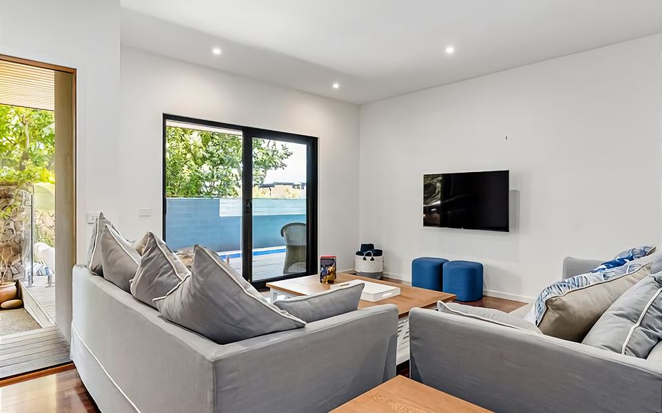 Downstairs lounge with comfy linen-upholstered couches, TV, and large sliding doors that open onto the pool side deck.