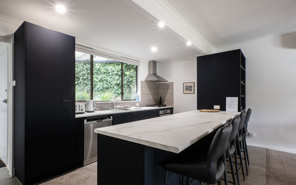 Kitchen with large breakfast bench, gas cooktop, oven, dishwasher, microwave, fridge and an abundance of cutlery, crockery, glassware, pots and pans, and a coffee plunger.