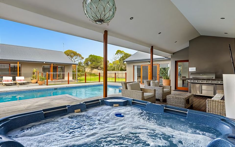 Solar heated swimming pool and hot tub spa beside a sundrenched deck and sheltered alfresco dining with gas mains BBQ, sun umbrella, and outdoor living area.